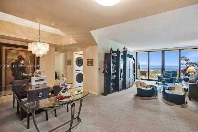 sitting room with baseboards, an inviting chandelier, stacked washer / drying machine, expansive windows, and carpet flooring