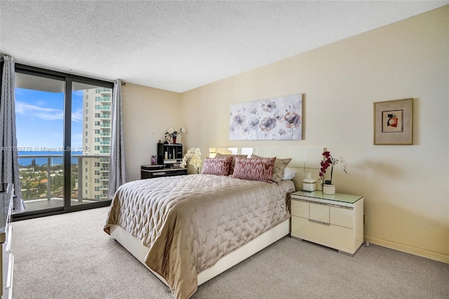 bedroom with access to exterior, a textured ceiling, carpet, and expansive windows