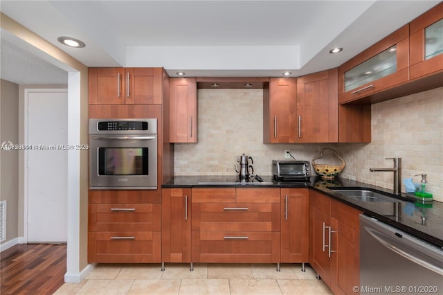 kitchen with backsplash, dark stone counters, brown cabinets, stainless steel appliances, and a sink