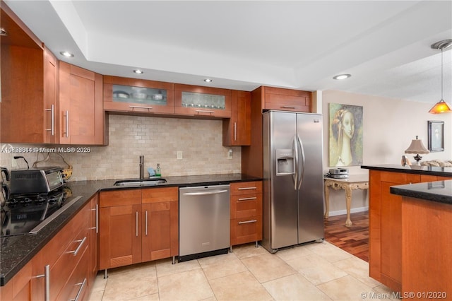 kitchen with brown cabinetry, a sink, stainless steel appliances, pendant lighting, and backsplash