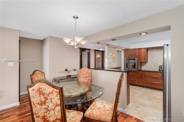 dining room featuring light wood-type flooring, baseboards, a textured ceiling, and an inviting chandelier