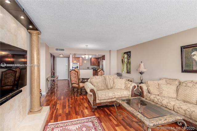 living room with wood finished floors, visible vents, decorative columns, a textured ceiling, and a notable chandelier