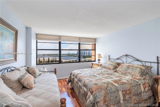 bedroom featuring baseboards, a water view, a textured ceiling, and wood finished floors