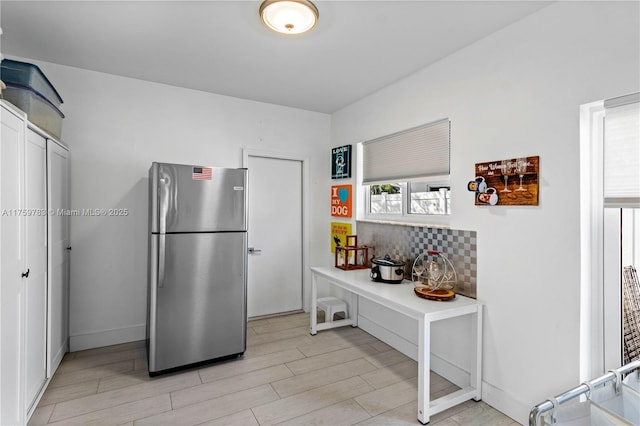 kitchen featuring decorative backsplash, baseboards, light wood-type flooring, and freestanding refrigerator