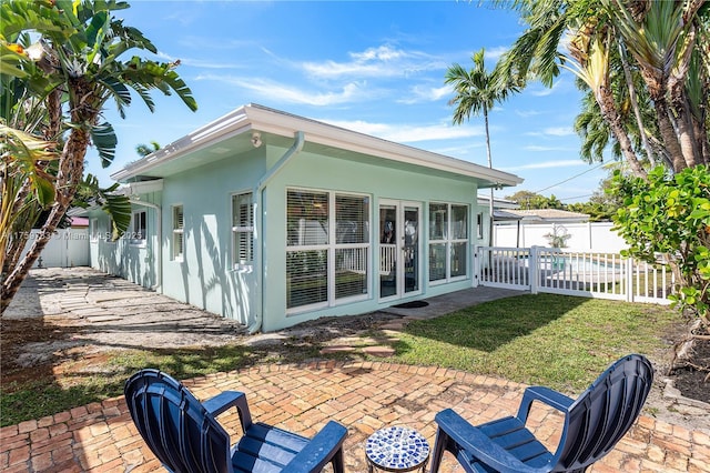 back of house featuring a patio, stucco siding, french doors, fence private yard, and a lawn