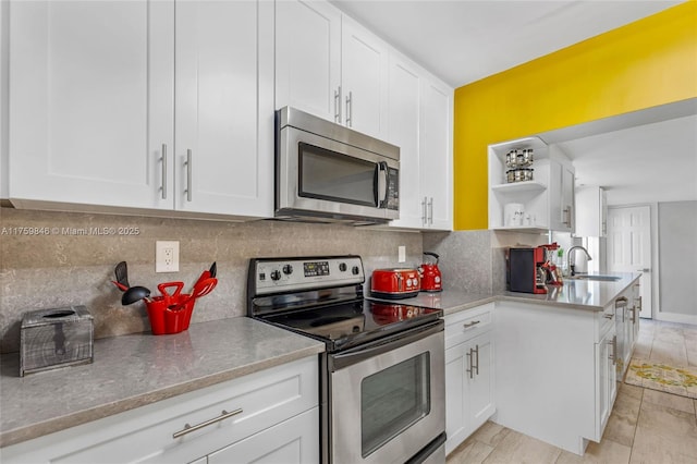 kitchen with white cabinetry, open shelves, stainless steel appliances, and a sink