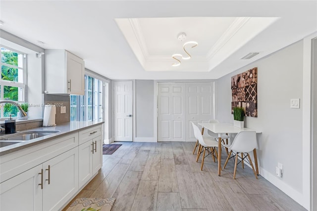 dining area featuring a raised ceiling, crown molding, baseboards, and light wood finished floors