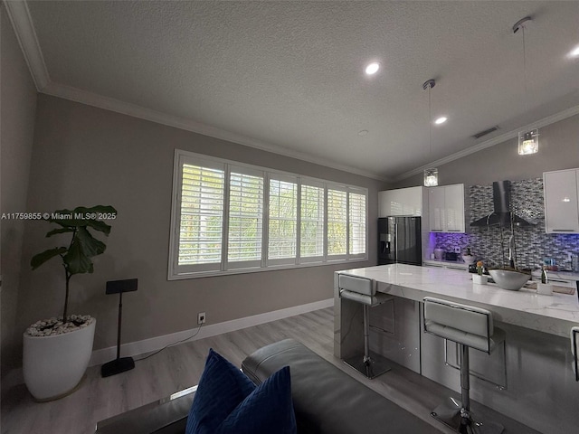 kitchen featuring ornamental molding, wall chimney range hood, black refrigerator with ice dispenser, and white cabinets