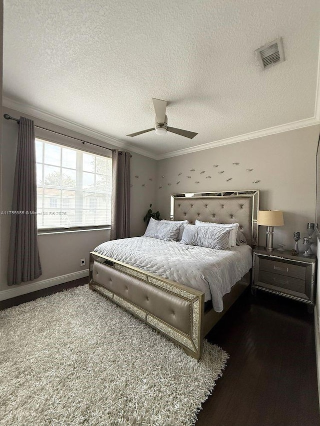 bedroom featuring a textured ceiling, wood finished floors, visible vents, baseboards, and ornamental molding