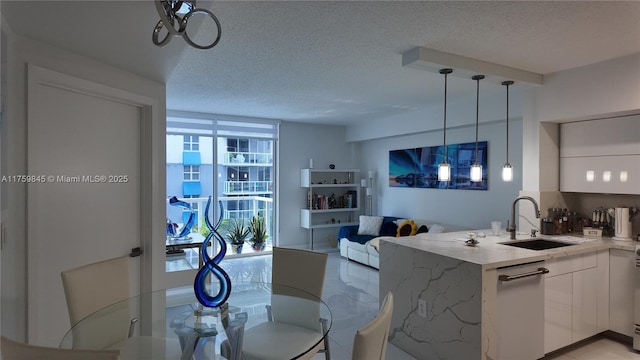 kitchen featuring a peninsula, a sink, a textured ceiling, white cabinetry, and decorative light fixtures