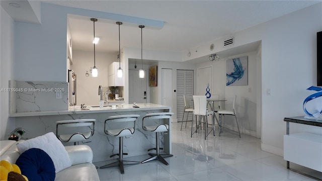 kitchen with visible vents, a breakfast bar, decorative light fixtures, white cabinetry, and a peninsula