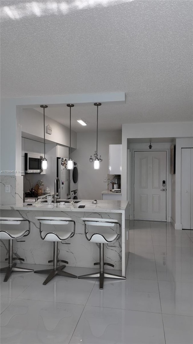 kitchen with a breakfast bar, stainless steel appliances, hanging light fixtures, white cabinets, and a textured ceiling