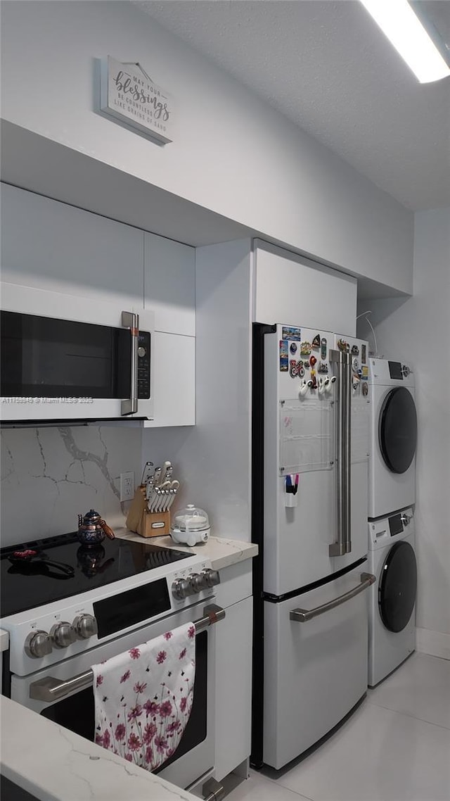 kitchen with stacked washer / drying machine, white appliances, backsplash, and white cabinetry