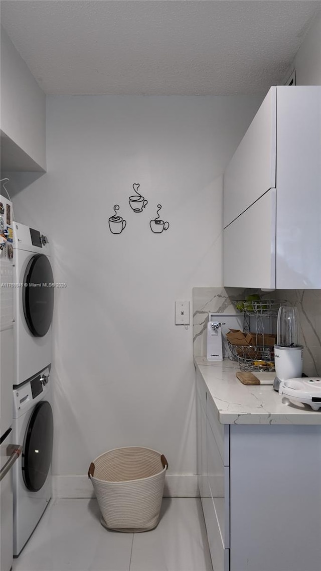 washroom featuring cabinet space, stacked washer / drying machine, and baseboards