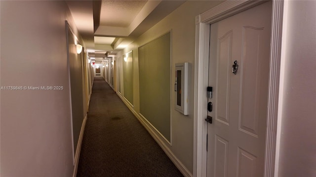 hall featuring dark colored carpet, a tray ceiling, and baseboards