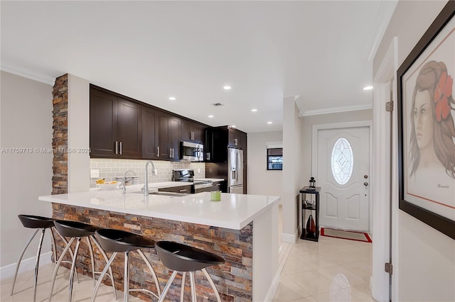 kitchen with appliances with stainless steel finishes, a breakfast bar, a sink, crown molding, and backsplash