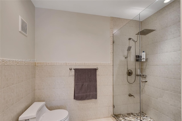 full bath with a wainscoted wall, tile walls, visible vents, toilet, and tiled shower