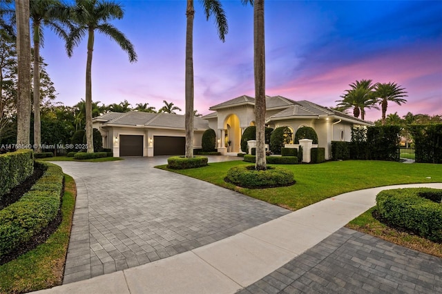 mediterranean / spanish-style house with stucco siding, a front lawn, a tile roof, decorative driveway, and a garage