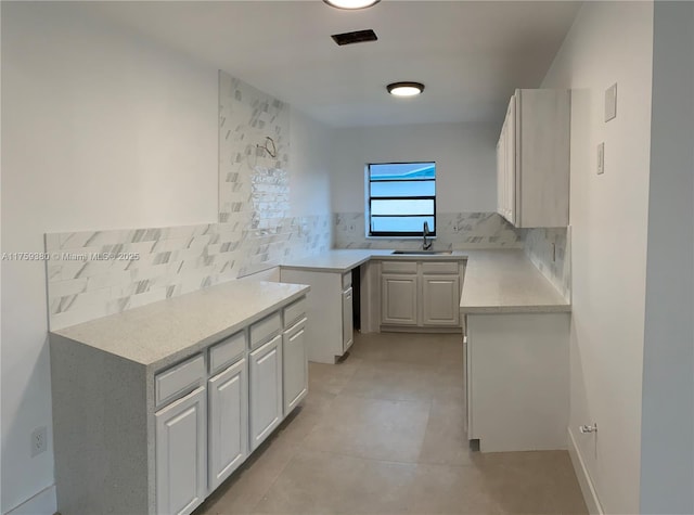 kitchen with a sink, backsplash, light tile patterned floors, and light countertops