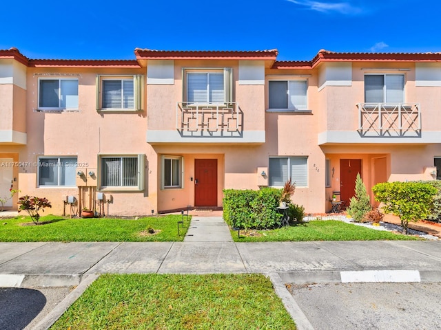 multi unit property with stucco siding, a front lawn, and a tiled roof