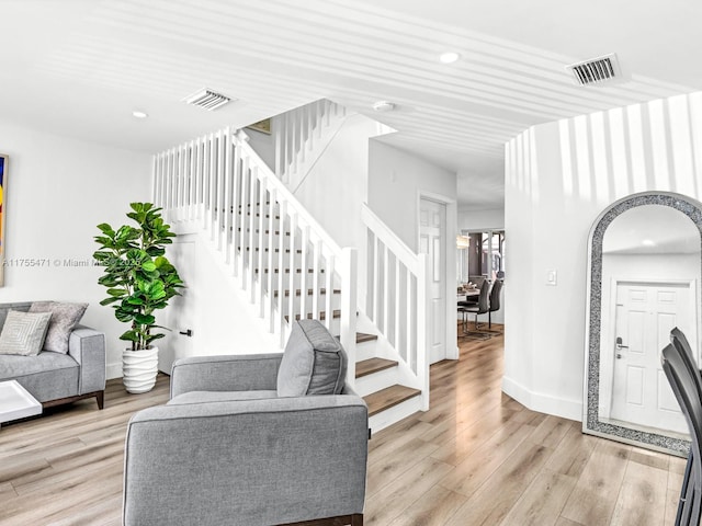 living room with stairs, light wood-style flooring, and visible vents