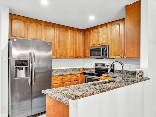 kitchen featuring brown cabinetry, stone counters, stainless steel appliances, and a sink