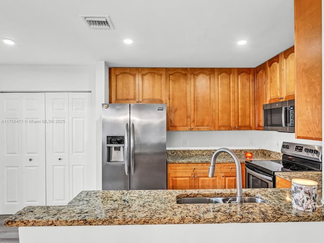 kitchen with a sink, visible vents, stone counters, and stainless steel appliances