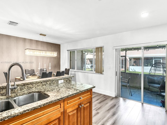 kitchen featuring a wealth of natural light, brown cabinets, light stone counters, and a sink