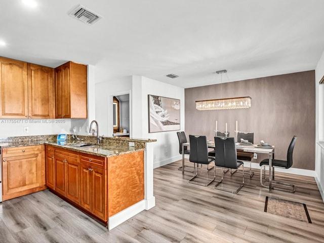 kitchen with visible vents, light wood-style flooring, a sink, light stone counters, and a peninsula