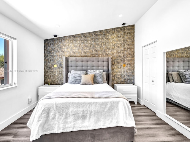 bedroom featuring a closet, baseboards, wood finished floors, and an accent wall