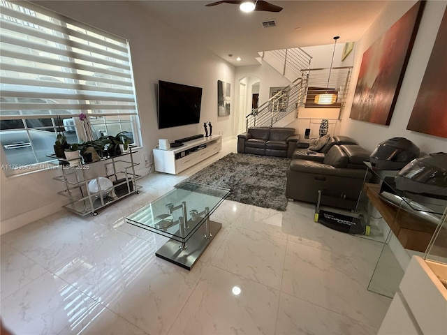 living area with a ceiling fan, stairway, visible vents, and marble finish floor