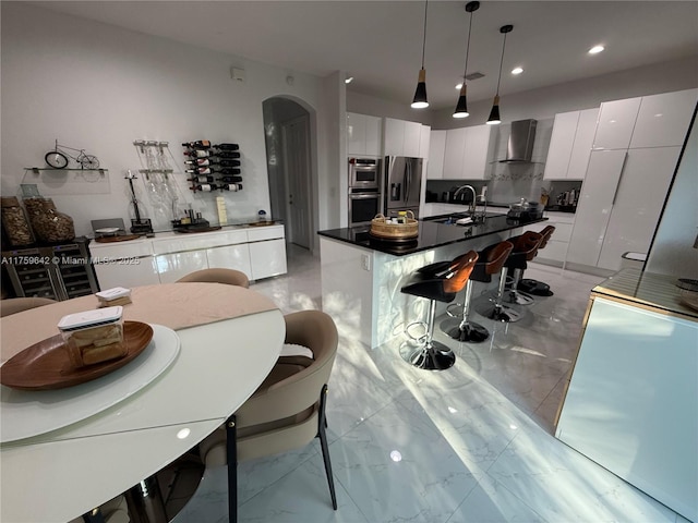 kitchen with modern cabinets, appliances with stainless steel finishes, white cabinets, and wall chimney range hood