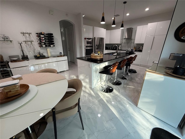 kitchen featuring dark countertops, wall chimney range hood, white cabinets, stainless steel appliances, and modern cabinets