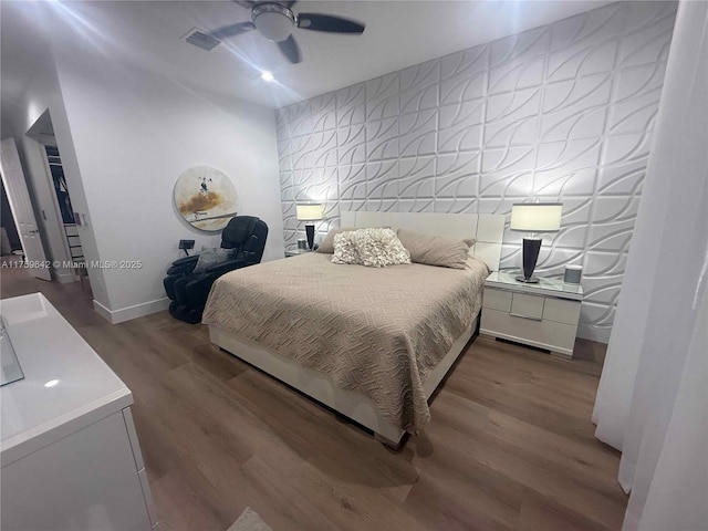 bedroom featuring visible vents, an accent wall, ceiling fan, baseboards, and wood finished floors