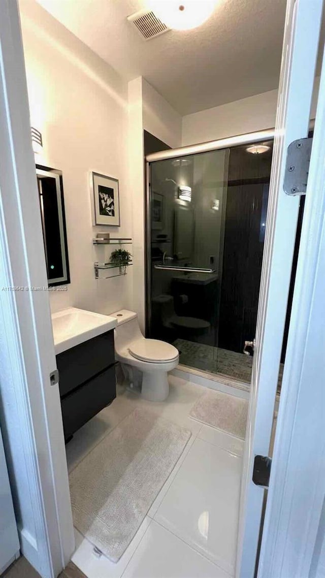 bathroom with tile patterned flooring, visible vents, a shower stall, toilet, and vanity