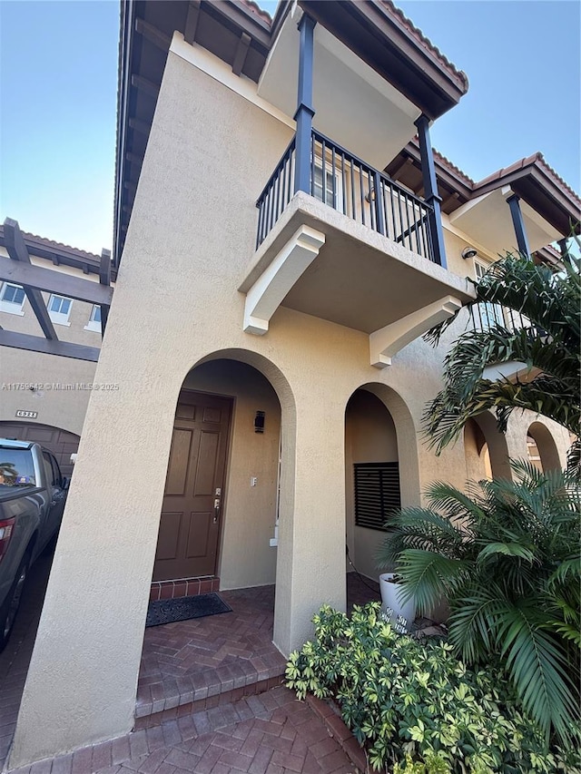 property entrance with stucco siding, a balcony, and a tile roof