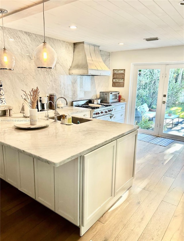 kitchen featuring light stone countertops, gas range oven, custom range hood, and a sink