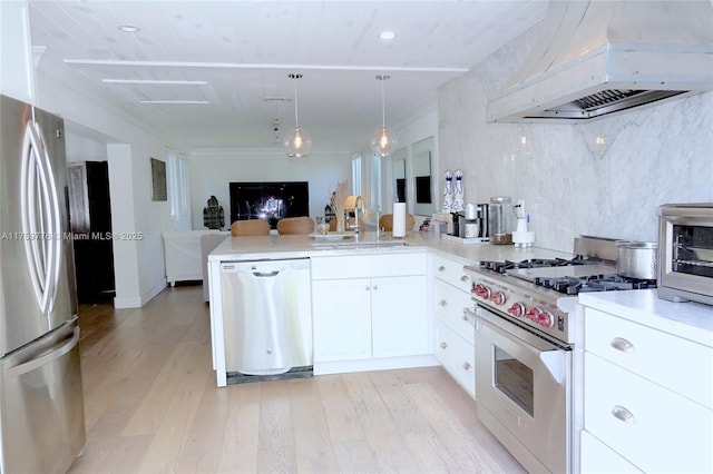 kitchen featuring appliances with stainless steel finishes, open floor plan, a sink, premium range hood, and a peninsula