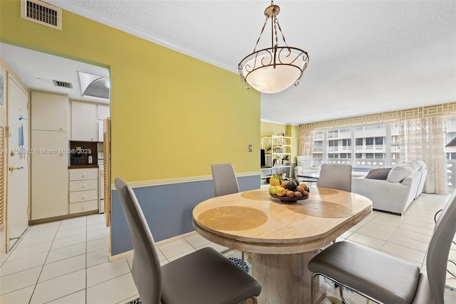 dining space featuring light tile patterned floors, visible vents, a textured ceiling, and crown molding