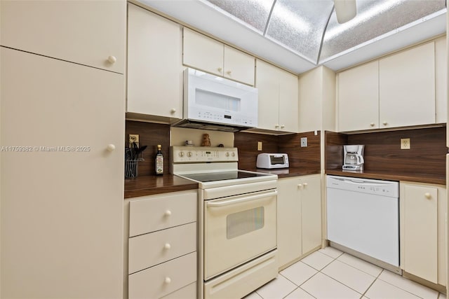 kitchen with white appliances, a toaster, light tile patterned flooring, white cabinets, and dark countertops