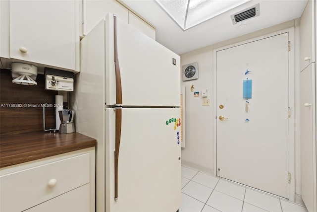 kitchen featuring dark countertops, visible vents, light tile patterned floors, freestanding refrigerator, and white cabinets