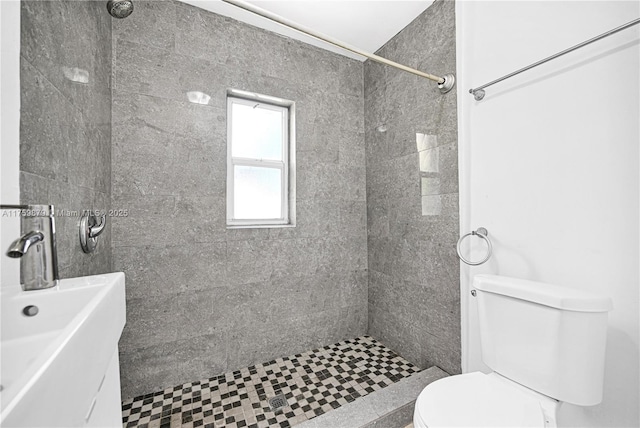 bathroom with a sink, tiled shower, and toilet