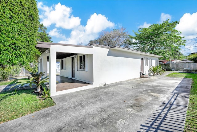 view of side of home featuring stucco siding, concrete driveway, a patio, and fence