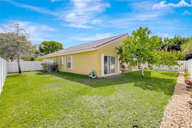 rear view of property featuring a tile roof, stucco siding, a lawn, and a fenced backyard