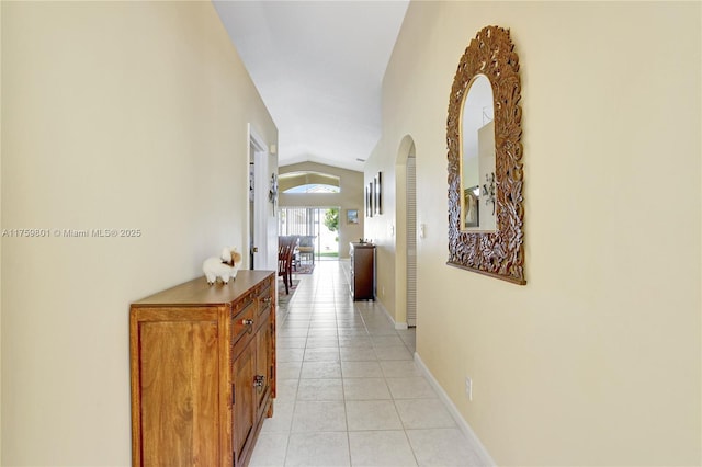 hallway with vaulted ceiling, light tile patterned flooring, baseboards, and arched walkways