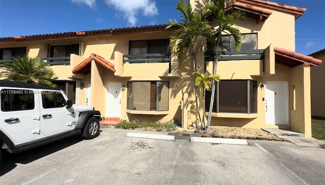 view of front facade featuring stucco siding, uncovered parking, and a tiled roof