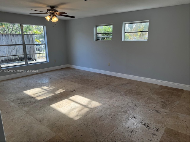 empty room with a wealth of natural light, baseboards, and ceiling fan