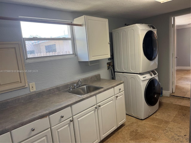 laundry room featuring baseboards, cabinet space, a sink, stacked washer / drying machine, and a textured ceiling