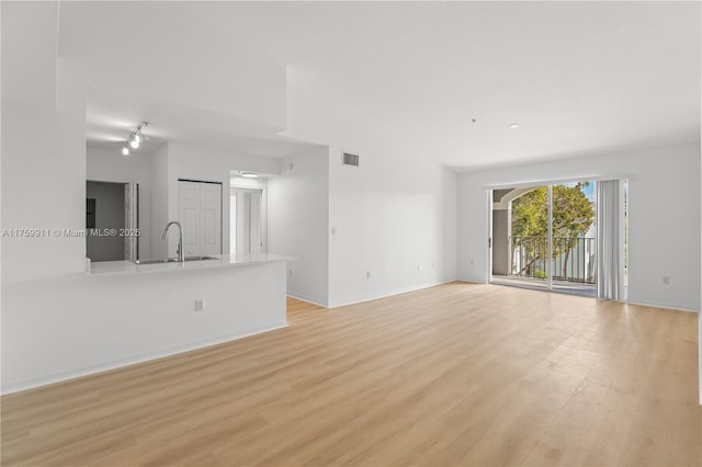 unfurnished living room featuring a sink, visible vents, baseboards, and light wood finished floors