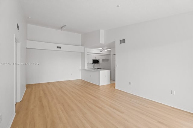 unfurnished living room with visible vents, vaulted ceiling, light wood-style flooring, rail lighting, and a sink